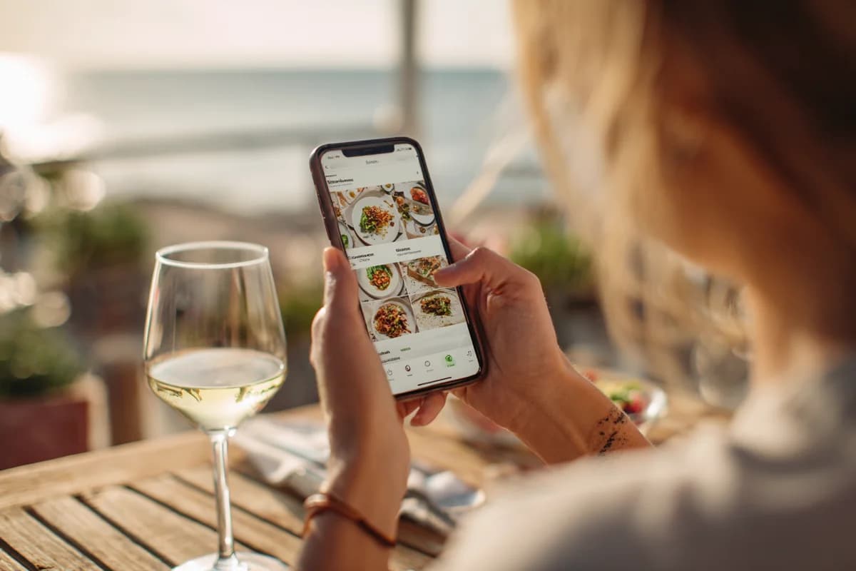 Cliente parcourant un menu digital interactif sur son smartphone en terrasse face à l'océan
